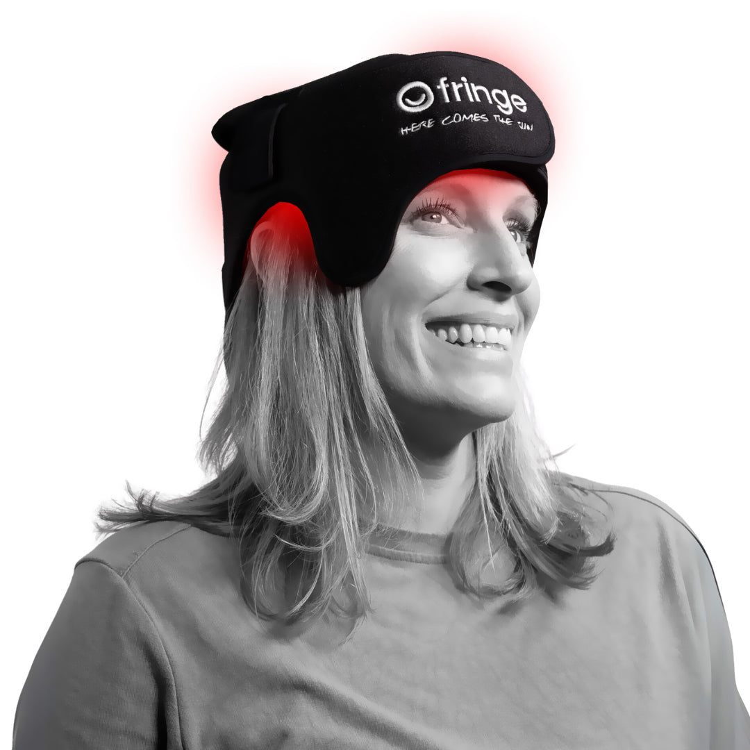 A woman smiles while wearing a black Fringe red light therapy head wrap with visible red LED lights.
