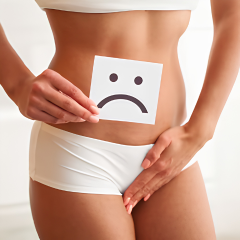 A person holds a sad face card over their lower abdomen, representing discomfort.